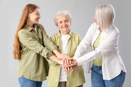 Young woman with her mother and grandma putting hands together on light backgroundの写真素材
