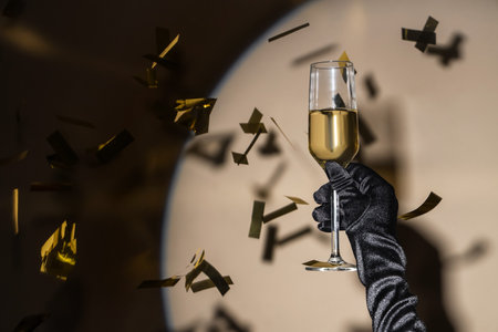 Female hand with glass of champagne and confetti on light backgroundの写真素材