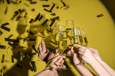 Female hands with glasses of champagne and confetti on yellow backgroundの写真素材