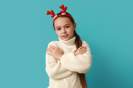 Cute little girl in reindeer horns hugging herself on blue backgroundの写真素材