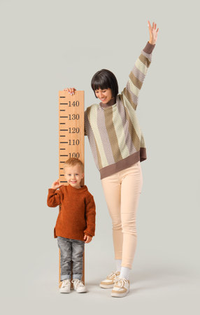 Young mother and her little son measuring height with stadiometer on light backgroundの写真素材