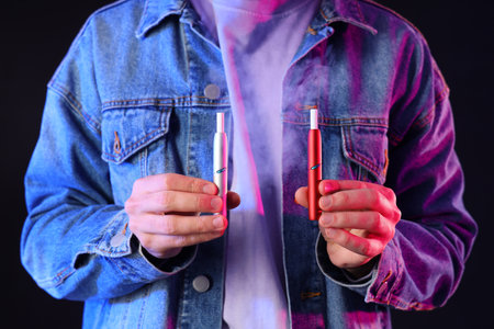 Young man with electronic cigarettes on dark background, closeupの写真素材