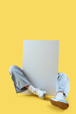 Female legs in stylish sneakers with blank advertising board on yellow backgroundの写真素材
