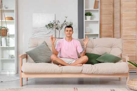 Young man meditating on sofa at homeの写真素材