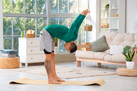 Sporty young man doing yoga on mat at home