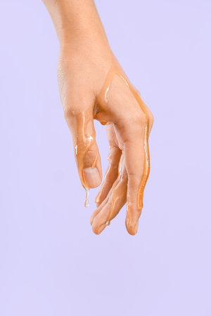 Woman with dripping honey on her hand against lilac backgroundの写真素材