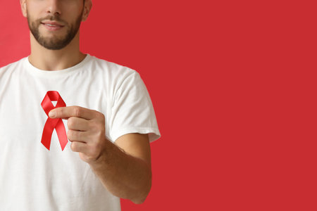 Man with red ribbon on color background. AID awareness concept