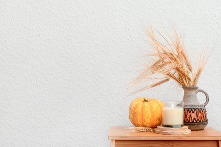 Spikelets of wheat, pumpkin and burning candle on wooden table near white wall, closeupの写真素材