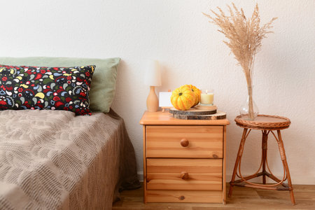 Wooden bedside table with burning candles, pumpkins and pampas grass in bedroomの写真素材