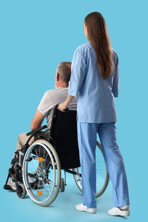 Senior man in wheelchair with nurse on blue background, back viewの写真素材