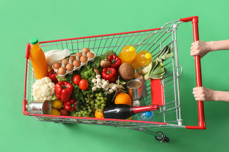 Woman pushing shopping cart full of different food on green backgroundの写真素材