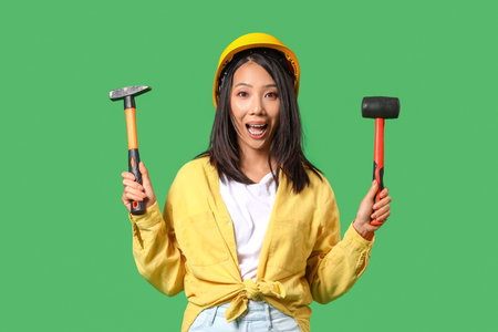 Young Asian woman with hammers on green background