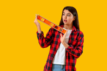 Shocked young woman with construction level on yellow background