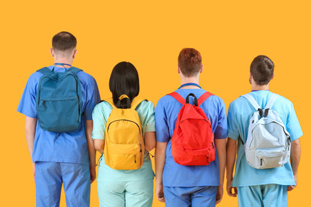 Group of medical students with backpacks on yellow background, back viewの写真素材