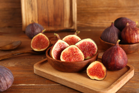 Board with fresh ripe figs and bowl of halves on wooden background