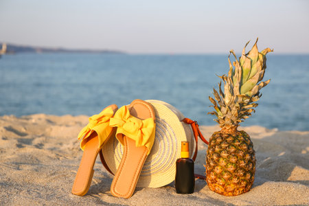 Stylish female sandals, bag, bottle of sunscreen and pineapple on sea beachの写真素材