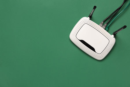 Modern wi-fi router with cables on green background