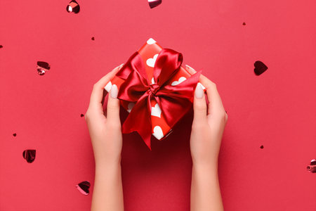 Female hands with gift box and confetti on red background. Valentine's Day celebrationの写真素材
