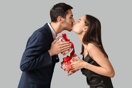 Beautiful young couple kissing with gift boxes on gray background. Valentine's day celebration
