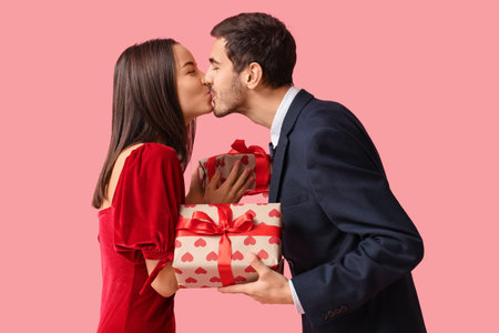 Beautiful young couple kissing with gift boxes on pink background. Valentine's day celebrationの写真素材