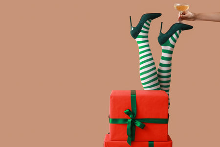 Female legs in Christmas stockings with glass of champagne and gifts on beige background. New year party conceptの写真素材