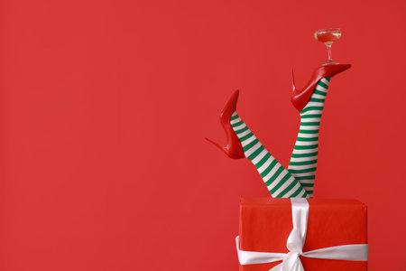 Female legs in Christmas stockings with glass of champagne and gift on red background. New year party conceptの写真素材