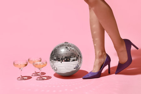 Female legs in high heel shoes with glasses of champagne and disco ball on pink background. New year party conceptの写真素材