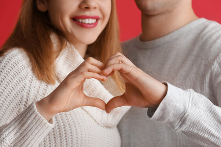 Lovely couple making heart with their hands on red background, closeup. Valentine's Day celebrationの写真素材