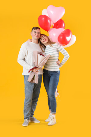 Lovely couple with bouquet of flowers and heart-shaped balloons on yellow background. Valentine's Day celebrationの写真素材