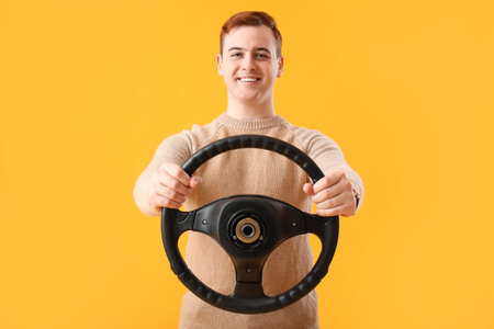 Young man with steering wheel on yellow background