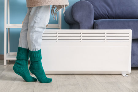 Young woman in winter socks with warm plaid near electric heater at home. Concept of heating seasonの写真素材