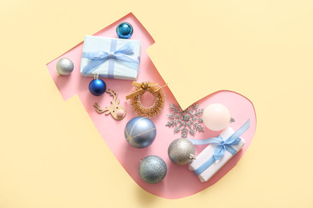 Cut yellow paper in shape of Christmas sock with balls and gifts on pink background