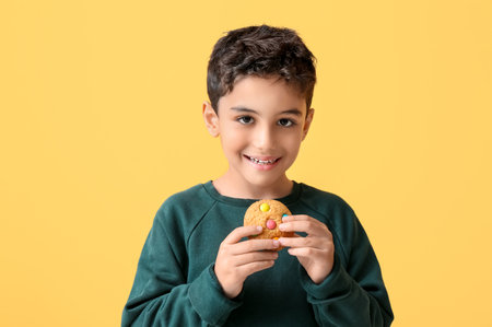 Cute little boy eating tasty cookie on yellow backgroundの写真素材