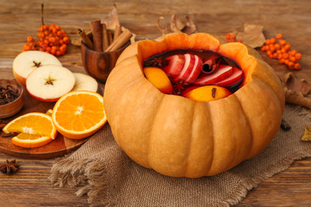 Tasty mulled wine in pumpkin with ingredients on wooden backgroundの写真素材
