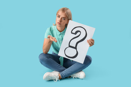 Young woman holding paper with question mark on blue backgroundの写真素材
