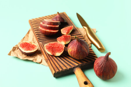 Wooden board with fresh juicy cut figs and knife on turquoise background