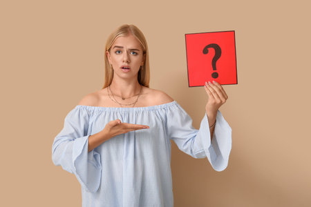 Confused young woman holding paper with question mark on beige backgroundの写真素材