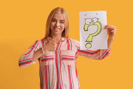 Young woman holding paper with question mark on yellow background