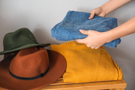 Woman stacking clean clothes on wooden table near light wall, closeupの写真素材