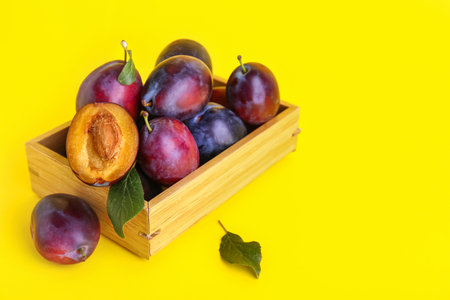 Wooden box with fresh ripe plums and leaves on yellow backgroundの写真素材