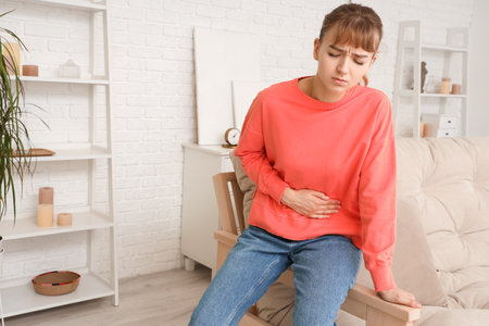 Young woman suffering from stomach ache at homeの写真素材