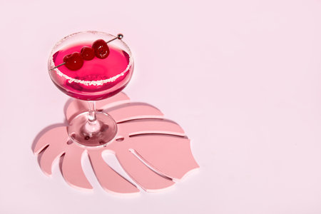 Glass of Cosmopolitan cocktail with cherries on pink backgroundの写真素材