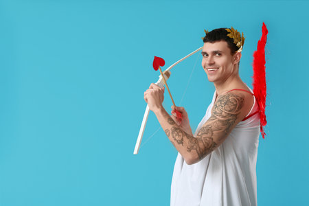 Young man dressed as Cupid with bow on blue background. Valentine's Day celebrationの写真素材