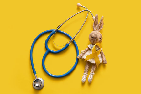 Golden ribbon with toy bunny and stethoscope on yellow background. Children cancer awareness conceptの写真素材