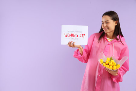 Young woman in raincoat with bouquet of tulips and card on lilac background. International Women's Dayの写真素材