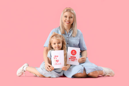 Little girl and her mother with greeting cards sitting on pink background. International Women's Day celebrationの写真素材