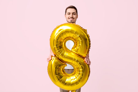 Young man with golden air balloon in shape of figure 8 on pink background. International Women's Dayの写真素材