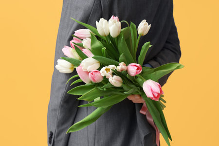 Young man with bouquet of beautiful tulips on yellow background. International Women's Dayの写真素材