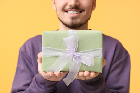 Young man with gift box on yellow background. International Women's Dayの写真素材
