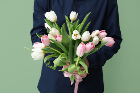 Young man with bouquet of beautiful tulips on green background. International Women's Dayの写真素材